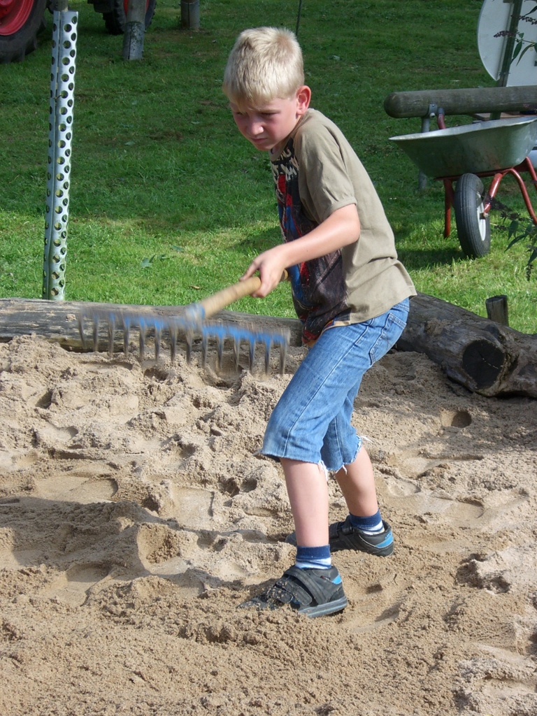 Kind verteilt neuen Sand auf dem Spielplatz